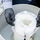 Gloved hands holding wastewater testing sample container