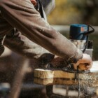 person in a brown long-sleeved top using a blue power tool on a workbench